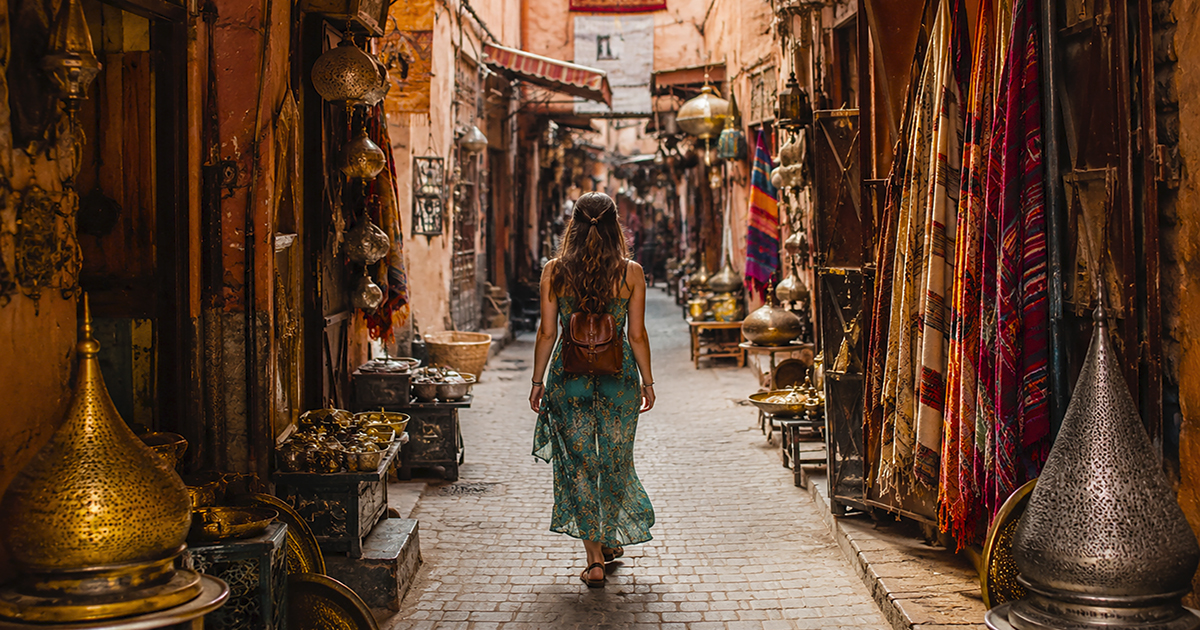 Viaggiatrice cammina in un souk della medina tra lanterne, tessuti e oggetti in ottone